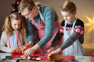 Fototapeta premium Happy father with his children bakes ginger cookies for Christmas with christmas tree on background