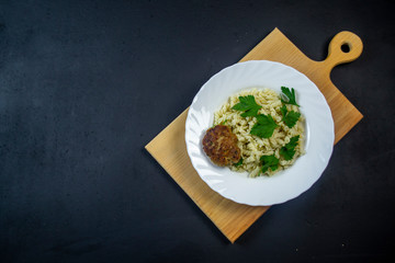 boiled pasta with meatballs on a white plate on a wooden board