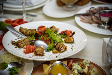 White ceramic plate full of slices of grilled eggplant decorated cucumbers and parsley lies on scratched dark concrete