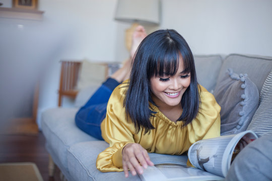 Woman lying on couch, reading magazine