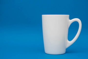 White ceramic cup on blue background. Space for text