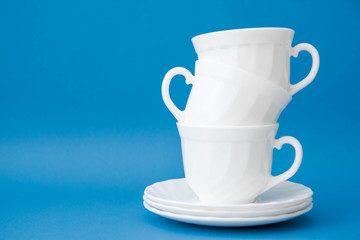 White ceramic cups with saucers folded pyramid on blue background. White tableware crockery set. Space for text