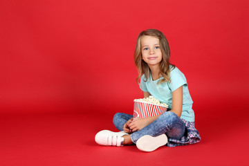 Obraz na płótnie Canvas Young girl with popcorn in bucket sitting on red background