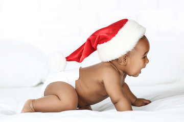 American baby girl in santa hat sitting on white bed