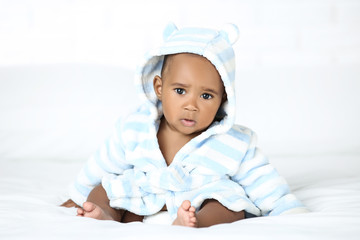 American baby girl in bathrobe sitting on bed