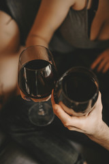 Two hands of man and woman holding glasses with red wine. Pleasant day with lovely people at home.