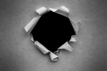 A hole in vintage paper with torn edges close-up with a black isolated background inside.