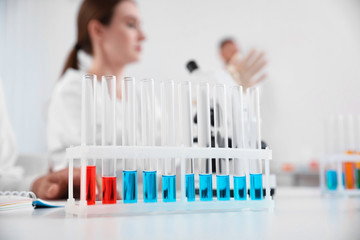 Rack with test tubes on white table and laboratory assistants in room. Medical research