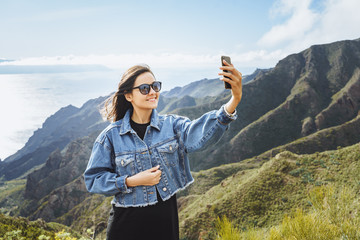 Young woman traveler taking a selfie using a smartphone on the background of the ocean and mountains.