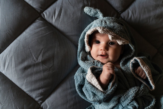 Portrait of baby girl lying on bed wrapped with shark shaped towel after bath
