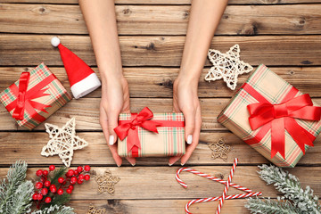 Gift box in female hands with christmas ornaments and fir tree branches on brown wooden table