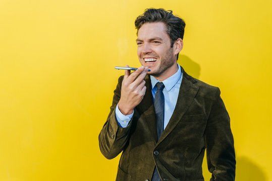 Happy businessman using smartphone in front of yellow wall