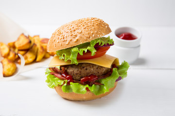 Fresh homemade burger with meat, ketchup and french fries on a light wooden background. Copy space.