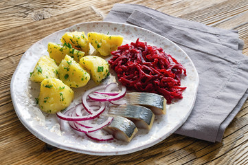 a meal of salted herring pieces, red onion half rings, potato chops with herbs and butter, and mayo beetroot salad with garlic 