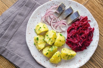 salted herring with potato and beetroot salad on a fleck ceramic plate on wooden background
