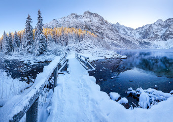 Wooden bridge covered with snow on mountain lake