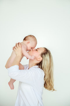 Photo of young beautiful mother with cute baby boy, smiling mommy lift her adorable son, pretty woman throwing up cheerful little child on white background, happy healthy family, love concept