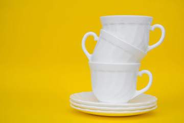 White ceramic cups with saucers folded pyramid on yellow background. White tableware crockery set. Space for text