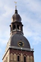 Riga, Latvia, November 2019. Tower of the Dome Cathedral with a golden weather vane against a cloudy sky.