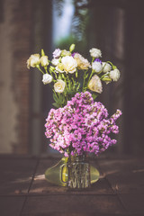 A bouquet of purple flowers in a glass vase on a wooden floor boards of old vintage.
