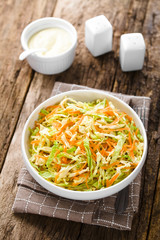 Coleslaw made of freshly shredded white cabbage and grated carrot in bowl, homemade mayonnaise-based salad dressing in the back (Selective Focus, Focus in the middle of the salad)