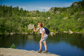 Tourist takes pictures of the mountains. Mountain lake and tourist with a camera. Girl with a backpack and a camera. Norway