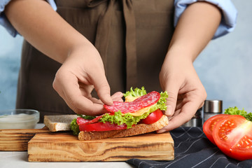 Obraz na płótnie Canvas Woman making tasty sandwich with sausage at table, closeup