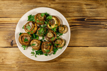Baked mushrooms in plate on wooden table. Top view