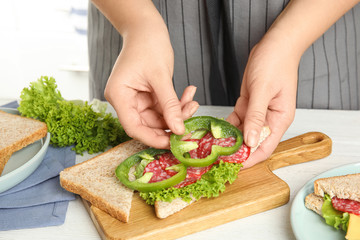 Woman making sandwich with green bell pepper and sausage at white table, closeup