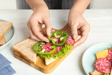 Woman making sandwich with green bell pepper and sausage at white table, closeup