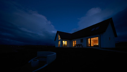 The warm glow of lit rooms from a remote Scottish Highland croft, bungalow at dusk in winter. - obrazy, fototapety, plakaty