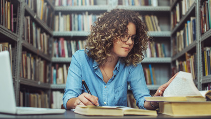 Young female student at the library. Young student reading book at library. Student learning for...