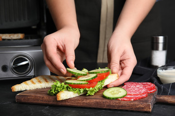 Woman adding cucumber to sandwich at black table, closeup