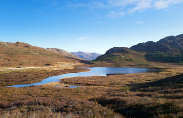 Views of Am Feur Loch in the centre and the A832 road on the left with Meall Lochan a Chleirich on the right on a sunny blue sky winters day in the Scottish Highlands.