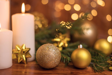 Golden Christmas ball on a tree branch, white candle flame with stars bokeh lights on a brown background