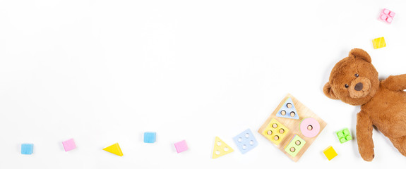 Baby kids toys banner background. Wooden educational geometric stacking blocks shape color recognition puzzle toy, teddy bear and colorful blocks on white background. Top view, flat lay