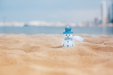 New Year's snowman in white in a blue hat on a background of a beautiful sea. Christmas and New Year holidays in the concept of warm countries.