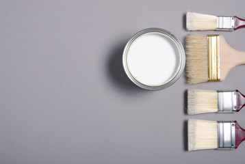 Open can with white paint and brush on gray background, top view. Space for text