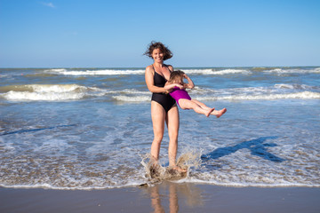 Fototapeta na wymiar Mother and daughter having fun on sea beach on summer vacation. Family on sea rest. Happy people in swimwear on beach