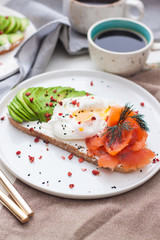 Toast with cream fresh, smoked salmon, poached egg and sliced avocado, and two cups of coffee. 