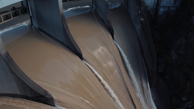 Close up turbulent fast water flows on dam floodgate overflow brown water after heavy rainfall