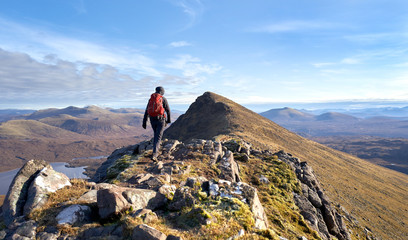 A hiker walking towards the summit of Sgurr an Tuill Bhain along a narrow rocky ridge in the...