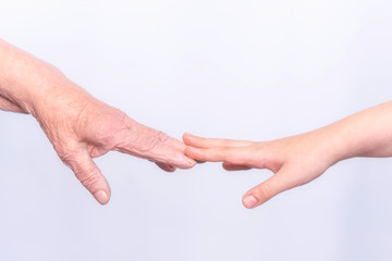 The hands of an old elderly grandmother and a child touch fingers in gestures on a white...