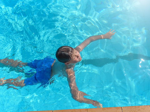 Learning to swim. Boy swimming along the side of pool.