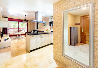 Entrance of a stylish bright kitchen with wooden cabinets next to the living room. Spacious modern fully equipped appliance interior with stone desk, ceramic stove and  big windows