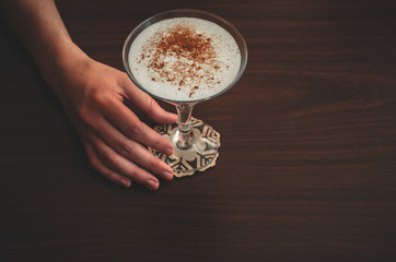 Female hand holds a glass of eggnog on wooden table background