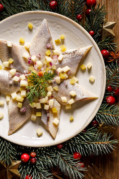 Christmas Herrings fillets with apples, pickled cucumbers, red onion and spices on a ceramic plate on a festive decorated wooden table, close-up, top view. Christmas, traditional dish
