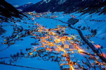 Winter night cityscape in the Austrian town of Neustift. Aerial view of the town center and the church. Night illumination of houses and traffic light. Tyrol, Stubai Valley