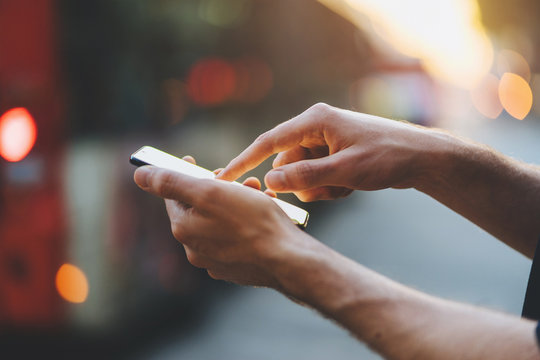 Close-up image of male hands using smartphone at the evening on city at the crossroads, searching or social networks concept, Man typing the messages on social network at the street with sunset 