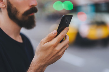 Attractive man with beard using smartphone while walking in city center, bokeh on the background